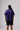 A back shot of a male model wearing the PONY Purple Striped Away jersey, black shorts, and PONY M100 sneakers standing in a studio.
