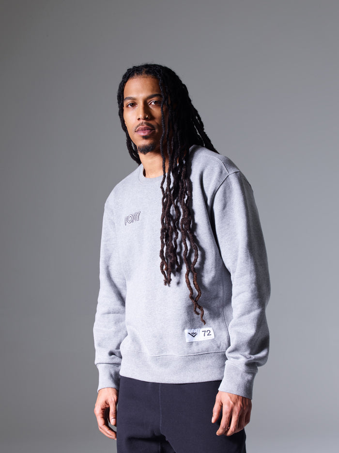 A male model wearing a heathered PONY Crewneck sweatshirt with Embroidered PONY word mark logo and PONY locker label with PONY Chevron and "72" sewn in bottom righthand corner.