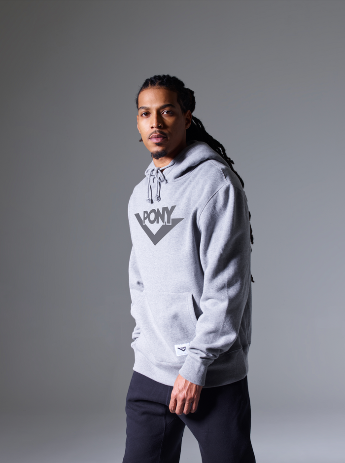 A male model wearing a PONY Classics Hooded Sweatshirt in Gray featuring a PONY Lockup on the front. The PONY Classics Sweatshirt also features a kangaroo pocket and PONY Locker label sewn on the bottom right. The Locker label shows a Black PONY Lock-up and "72" for 1972.