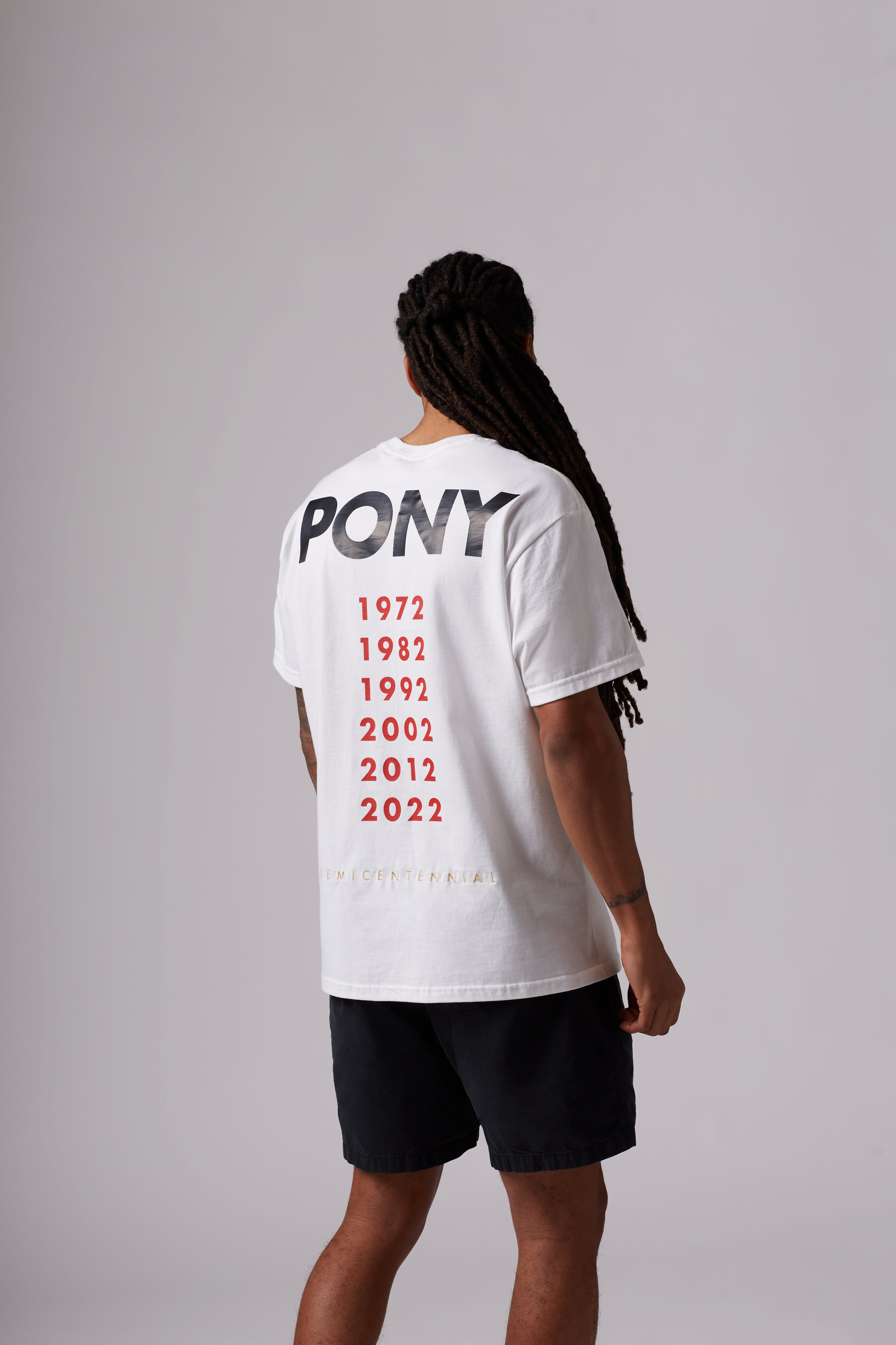 A back shot of the white semi centennial sports tee featuring a PONY word mark across the top and years printed in red below, Yellow embroidered "SEMICENTENNIAL" across the bottom.